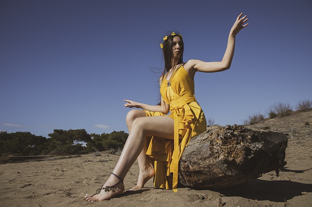 Žena v žltých šatách sedí na skale v púšti 